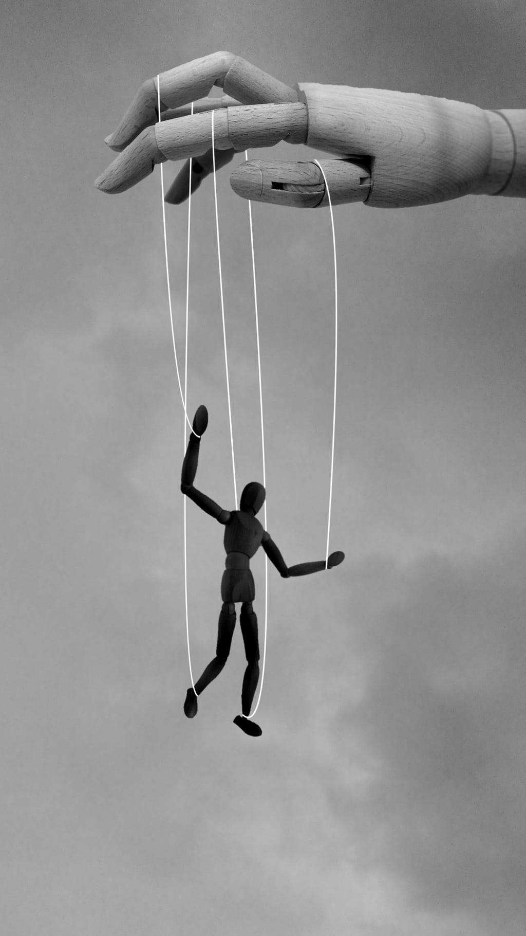 A wooden puppet on strings is controlled by above by a wooden hand.