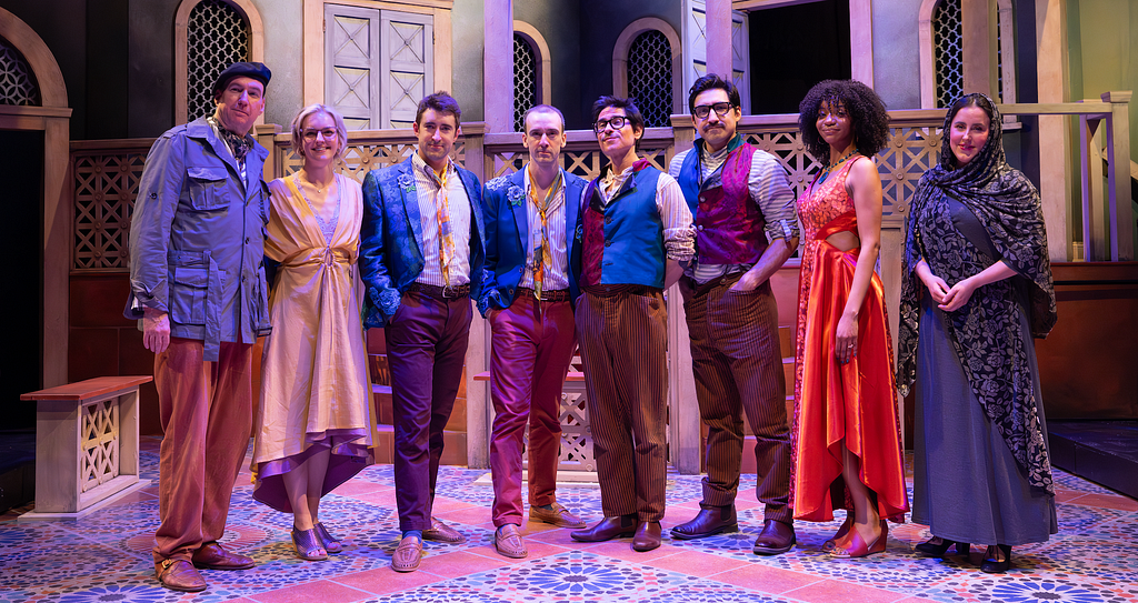 The cast of THE COMEDY OF ERRORS stands on a stenciled floor together and smiles.