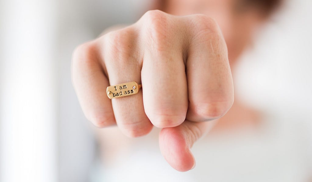 Photo of a fist wearing a ring that says, “I am badass.”