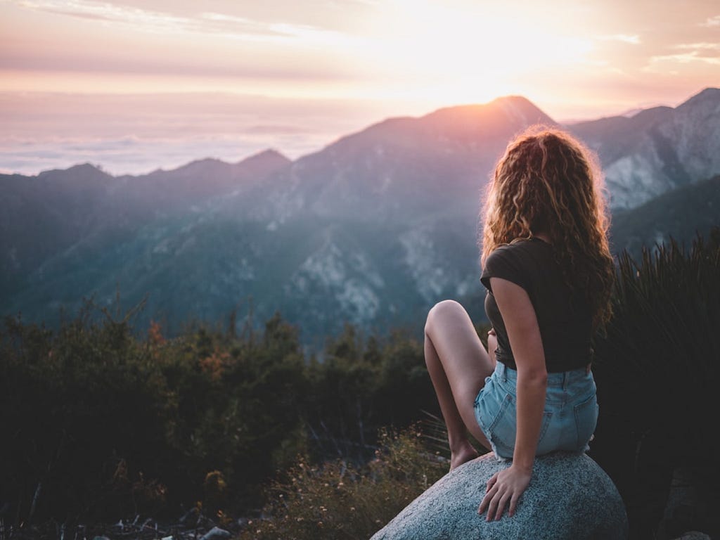 A girl sitting on a rock looking over the sun rise over the hills