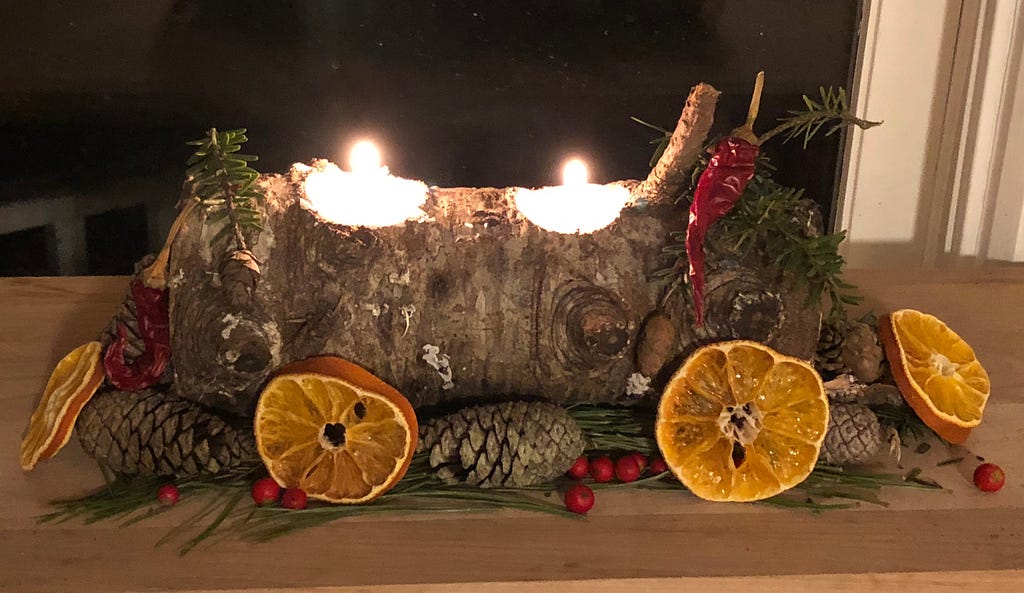 Yule log with bright candles, peppers, and dried oranges.