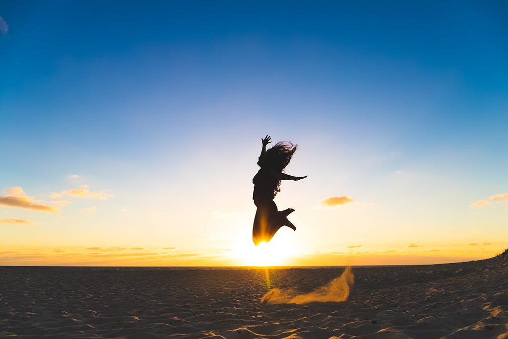 a woman jumping in joy with the sunrise as her background to represent the benefits of work-life balance