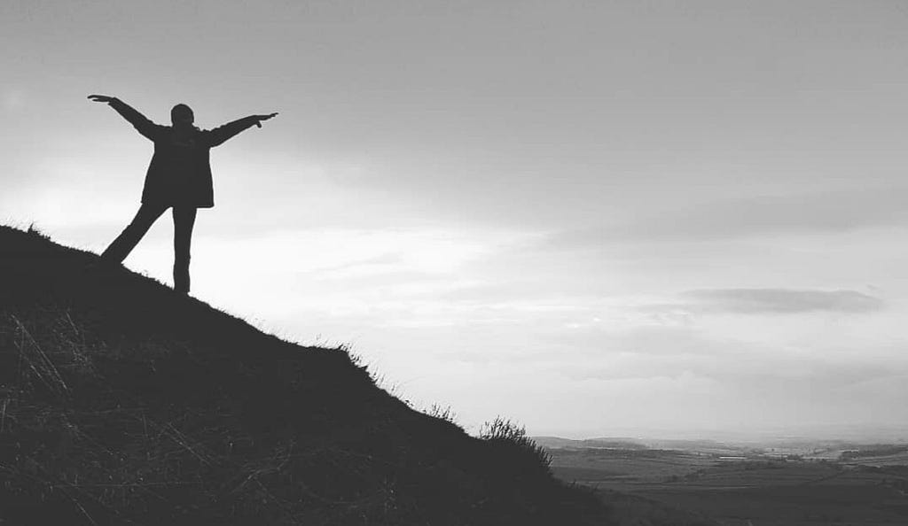 Woman standing on a hillside withher arms outstretched to meet the sunrise