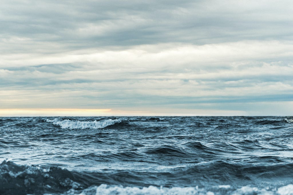 Small ocean waves crash with a backdrop of a sky filled with clouds.