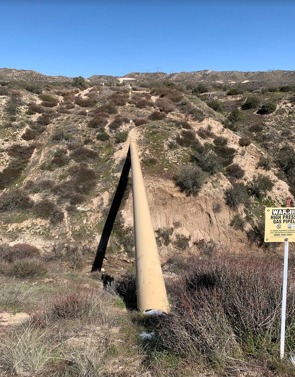 Round sand-colored gas pipeline stretching across a small ravine