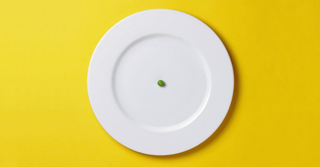 A white plate with a single green pea in the middle