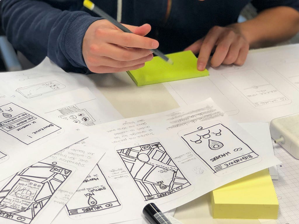 Close-up of a designer’s hands arranging paper sketches and sticky notes on a table during a brainstorming session, symbolizing the hands-on and creative aspects of the design process.