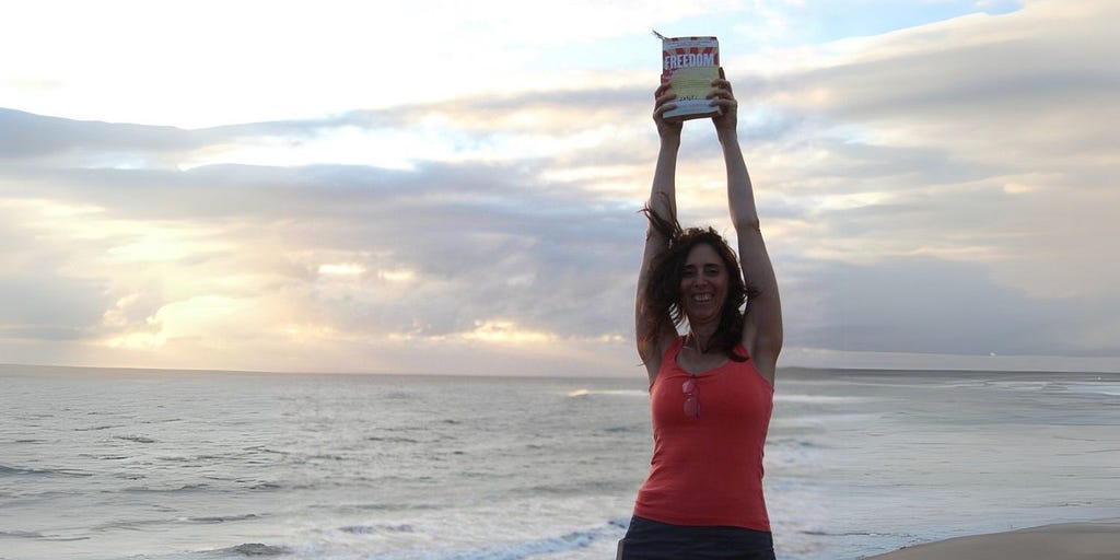 Woman on beach holding ‘FREEDOM’ by Jeremy Griffith above her head in joy