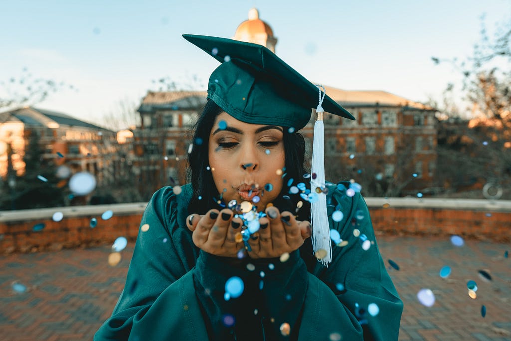 Young woman at graduation blowing confetti. Image taken from unsplash.