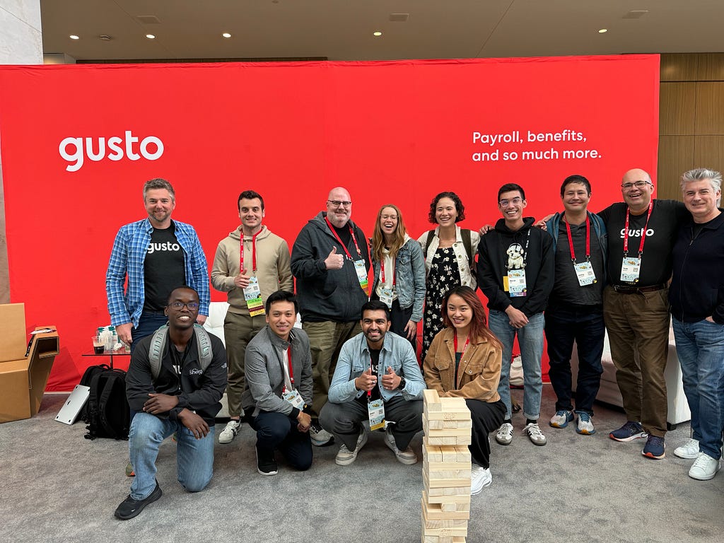 Several people gathered to take a picture in front of a guava-colored Gusto backdrop at RailsConf.