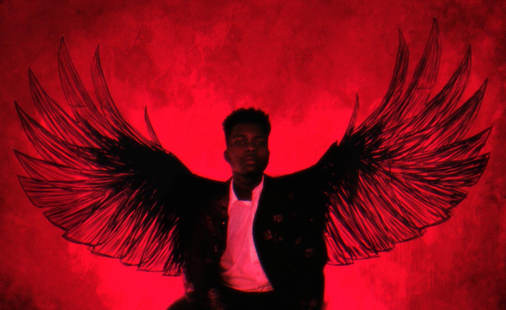Jhariah, a young Black man, is the central focus against a red background with illustrated crow wings.