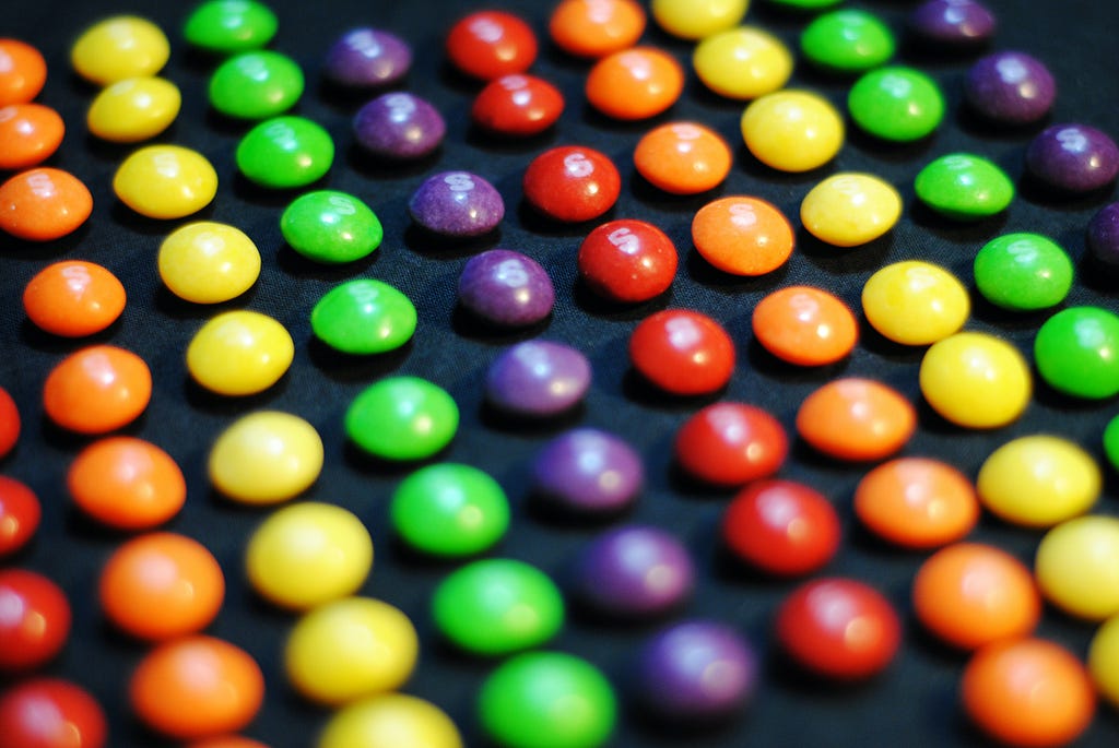 Rows of Skittles candy arranged by color on a black background.