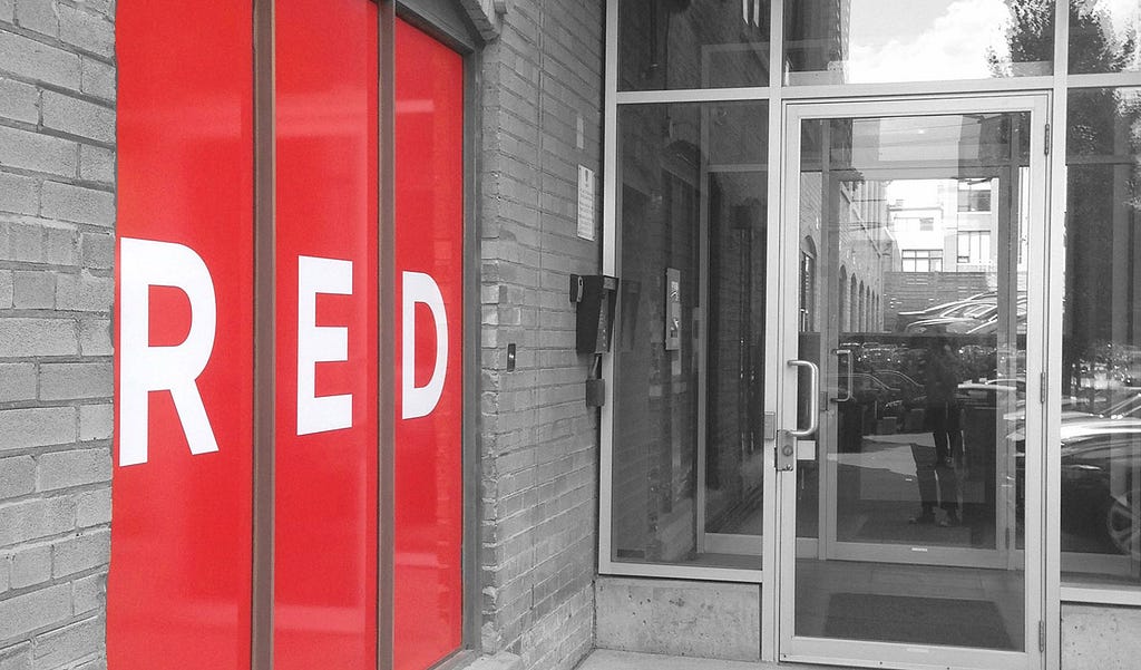 The entrance of RED Academy Toronto picturing a RED Academy’s iconic red and white logo in vinyl graphics on the window.