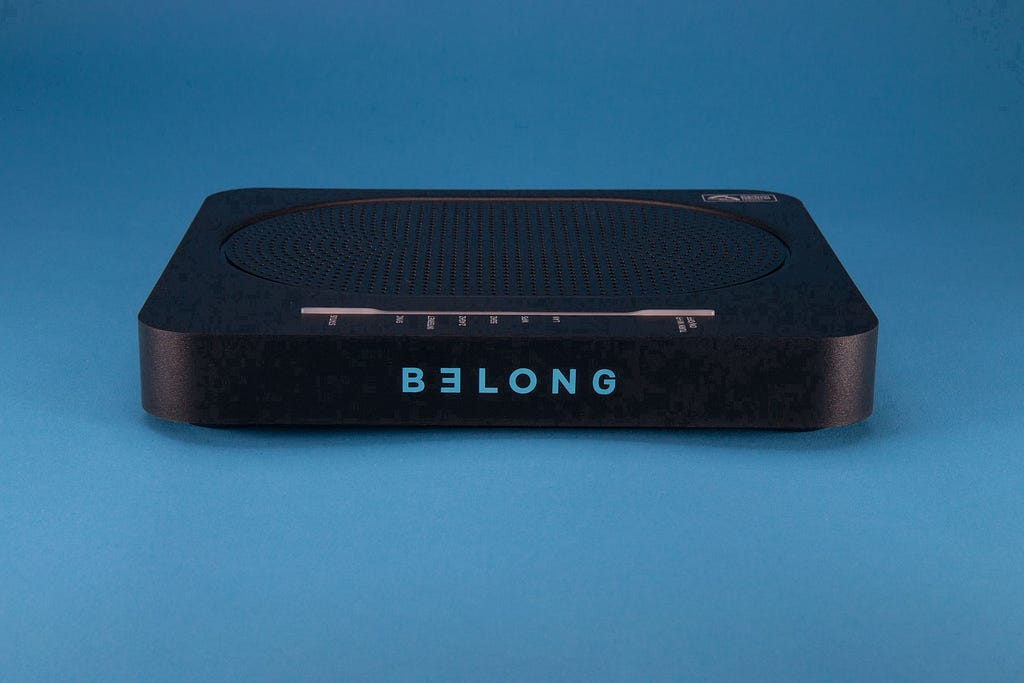 A black rectangualr internet modem labelled ‘BELONG’ sits on a blue background.