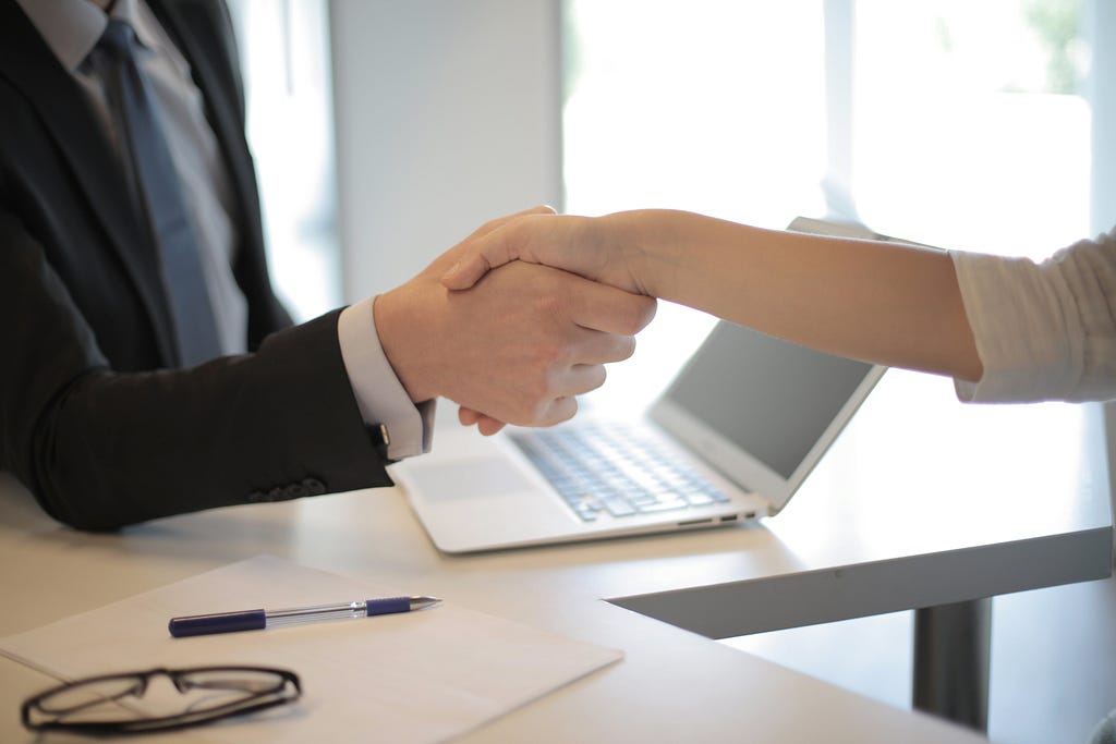A picture of a white man shaking a white woman’s hand at a job interview. Learn what questions to ask at the end of an interview.