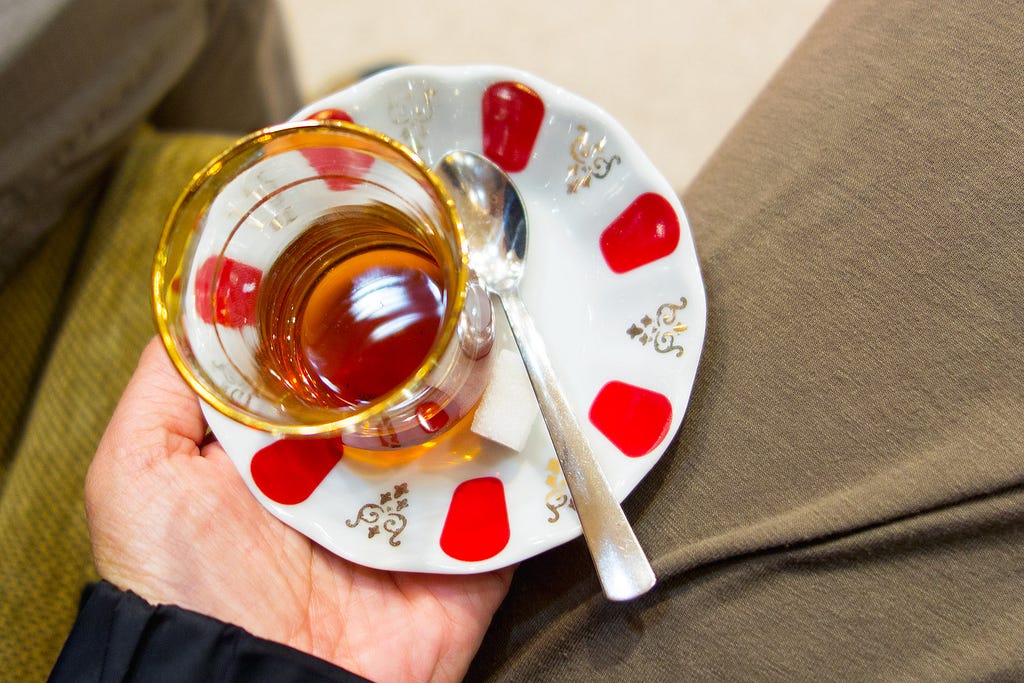 a ladies hand hold a tea cup and saucer with a spoon