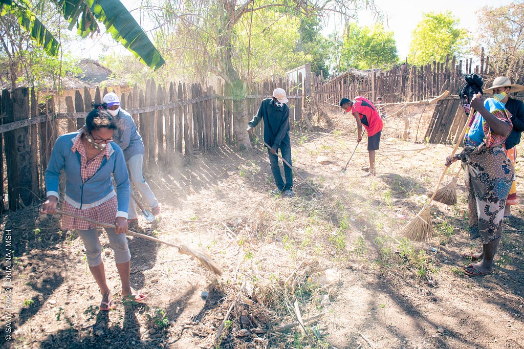 several people rake vegetation in a yard enclosed by a wooden fence