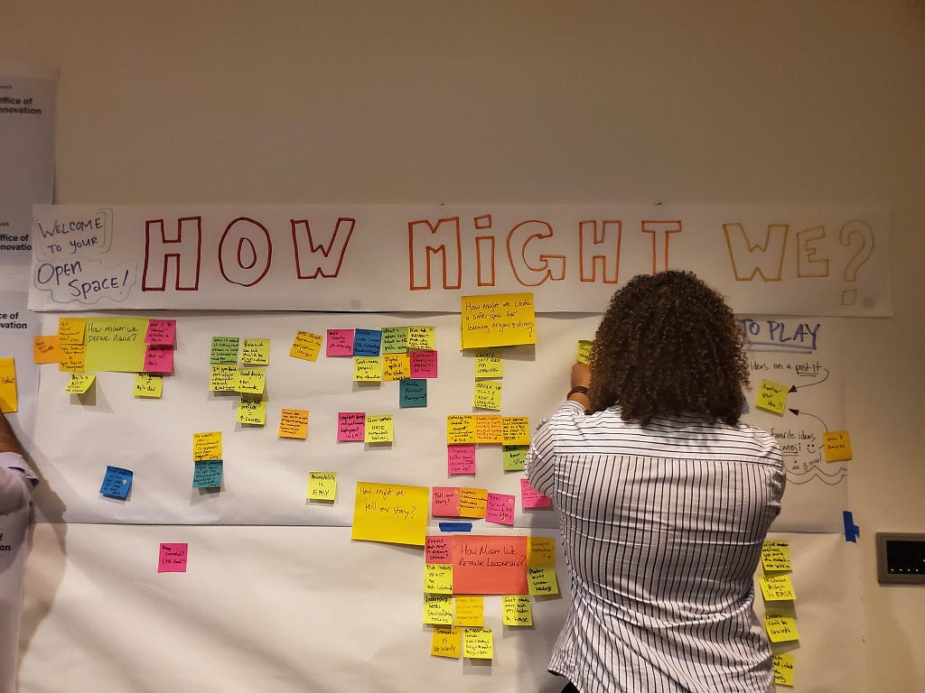 A young man adding a sticky note to a wall full of “how might we” stickies.