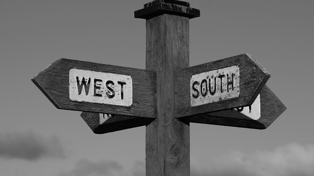 Rustic wooden signage showing west and south directions, in a sky’s background.