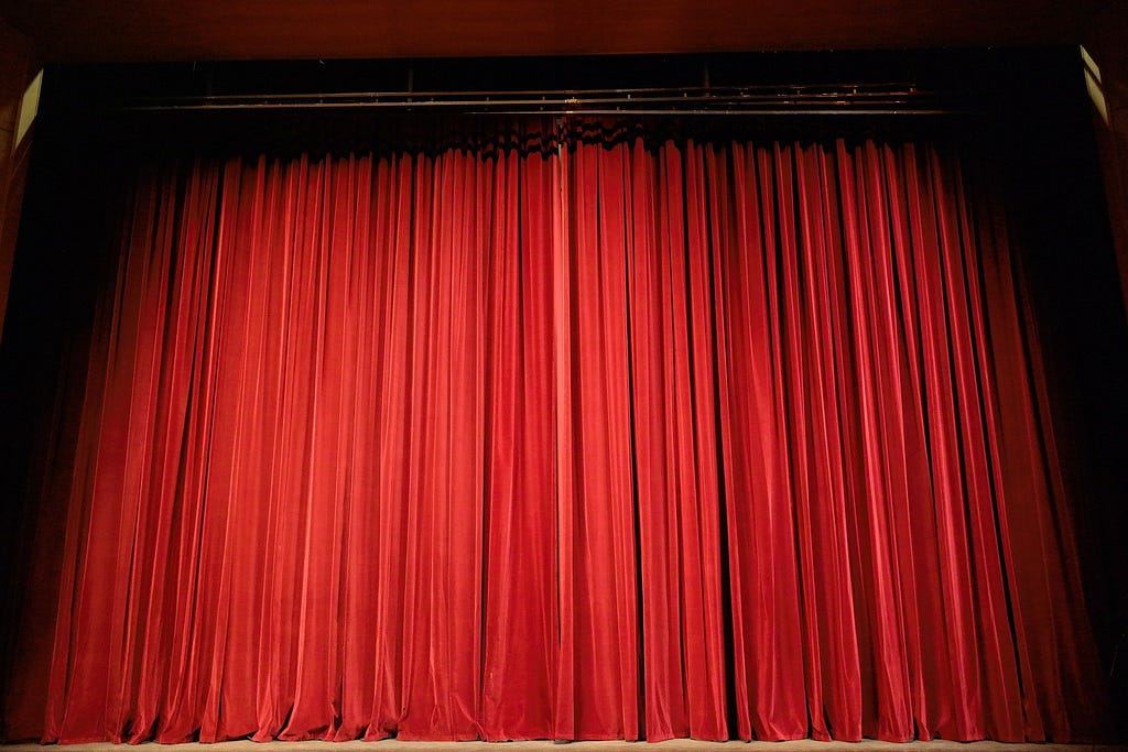 A bright, red theater curtain, closed.