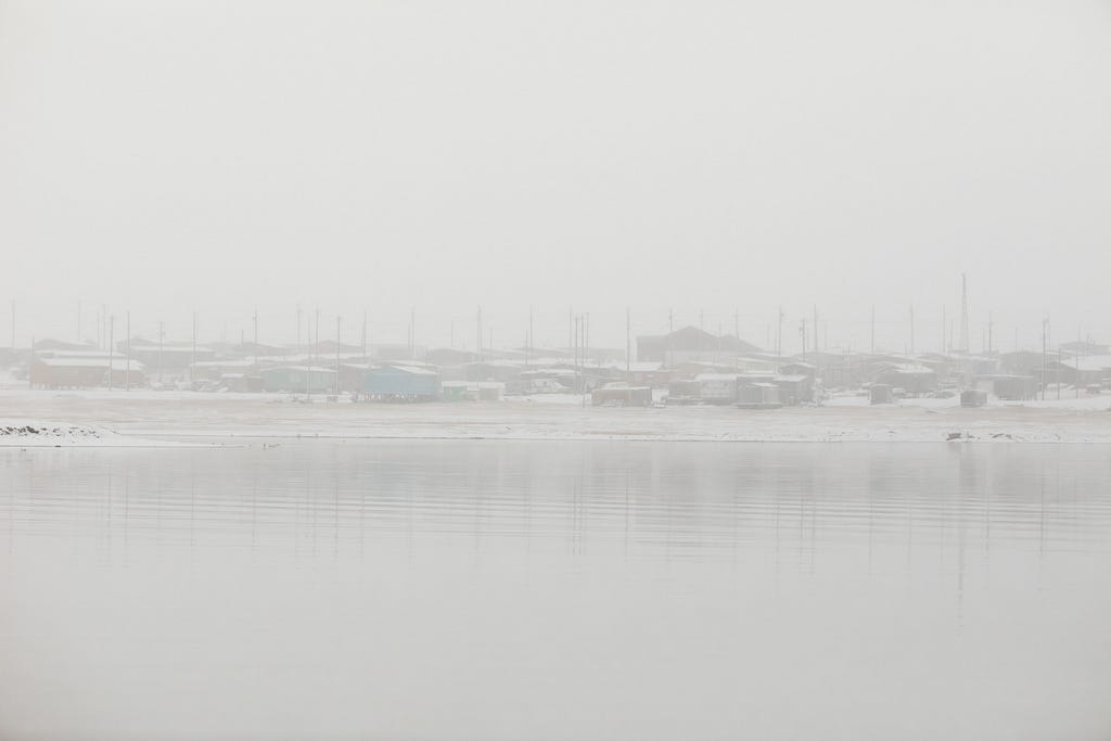 A foggy landscape photo of a cluster of buildings on the shore of a calm sea.