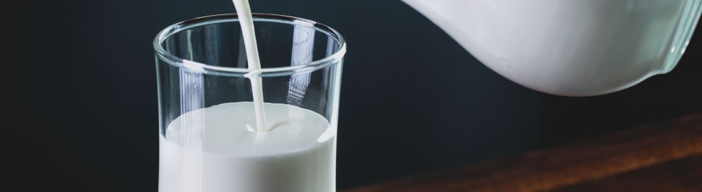 Milk being poured from a glass jug into a glass tumbler.