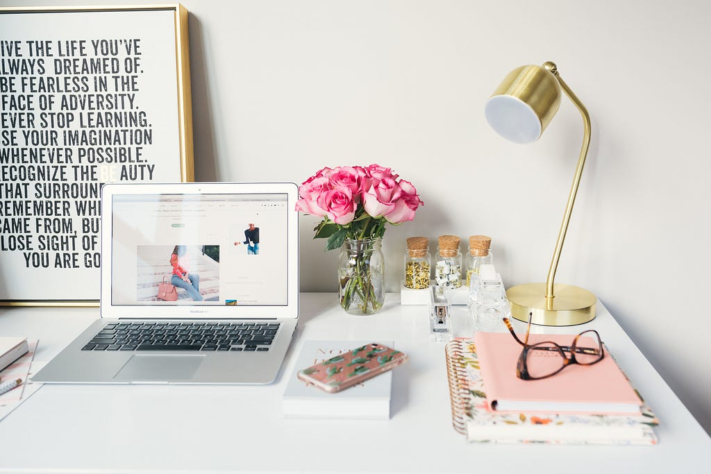 A highly organized desk with a laptop, flowers, desk lamp, eyeglasses, and various books and notepads.