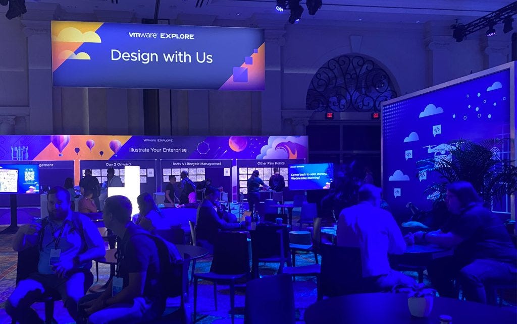 The Design with Us — Illustrate your Enterprise installation in the Explore Hub area was a wide open area with boards on the walls, monitors explaining what was happening and people at tables in a room with purple lighting.