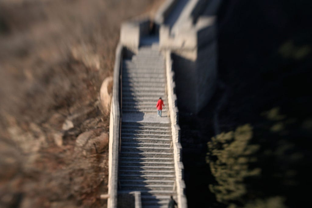 Woman in a red coat walking up the stairs of the Great Wall of China.