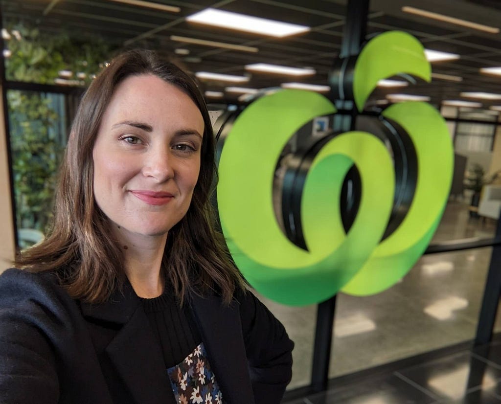 Rachael Harwood (the writer) smiling in a selfie at the Countdown head office with a large green Countdown logo in the background