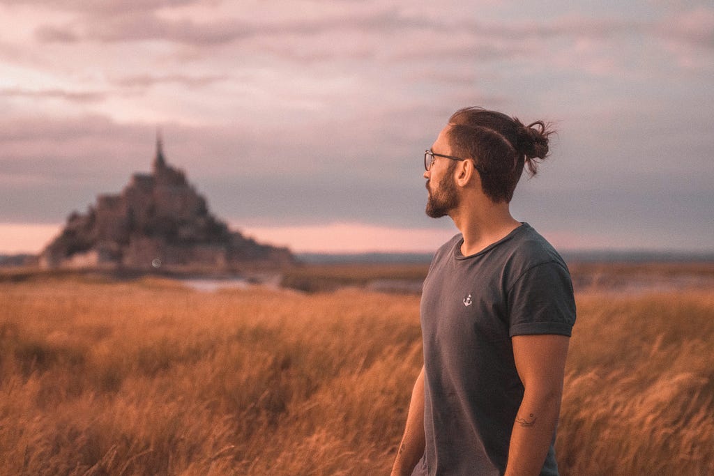 Man standing in a field and looking out at a castle at dawn