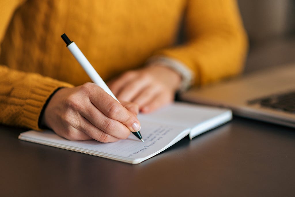 A person wearing a yellow sweater writes on a notebook.