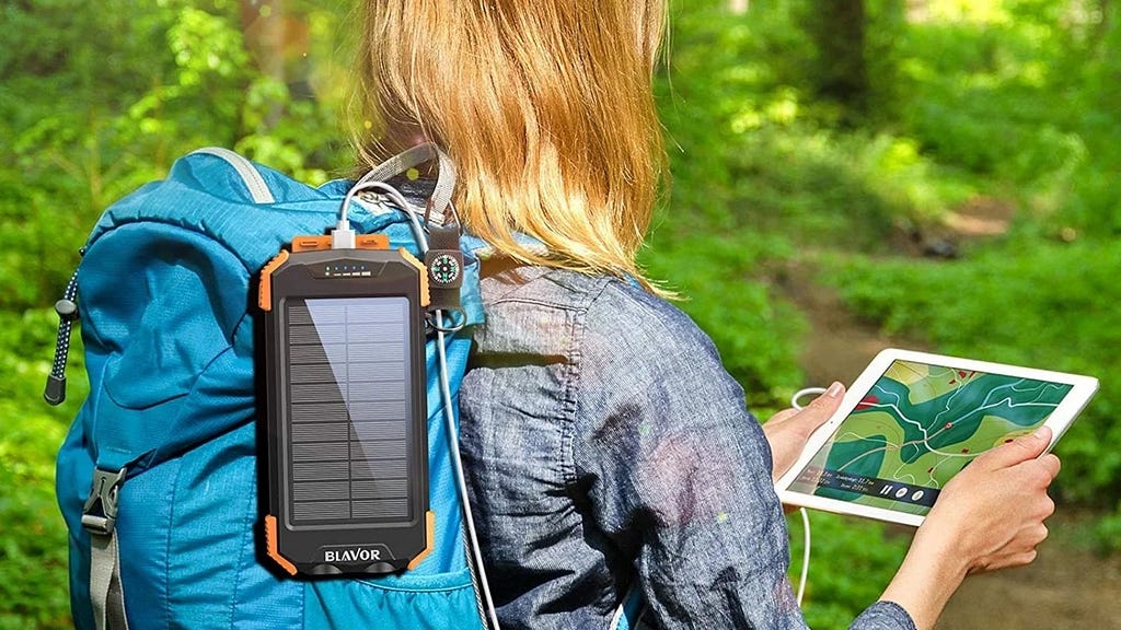 Woman hiking and looking at a map on her electronic tablet that is plugged into a portable back-up battery power device on her backpack.