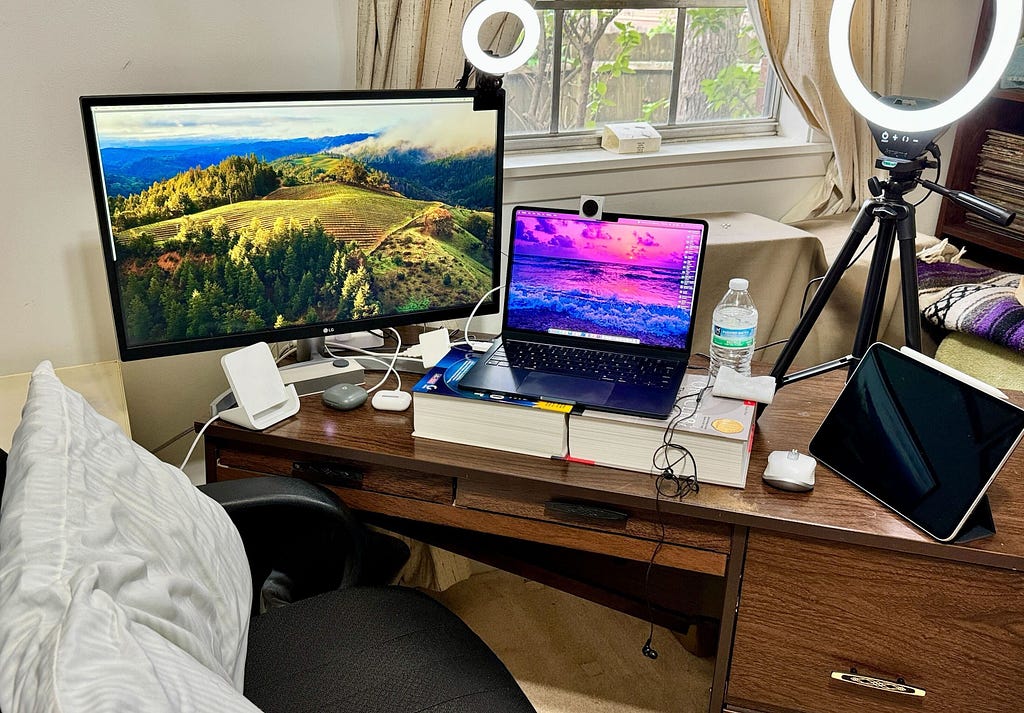 Multi-monitor setup with Macbook Air and iPad Pro with two ring lights, mouse, water bottle, headsets, and iPhone cradle