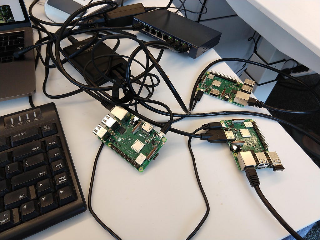 3 Raspberry Pi computers and a mess of cables on a desk next to a keyboard