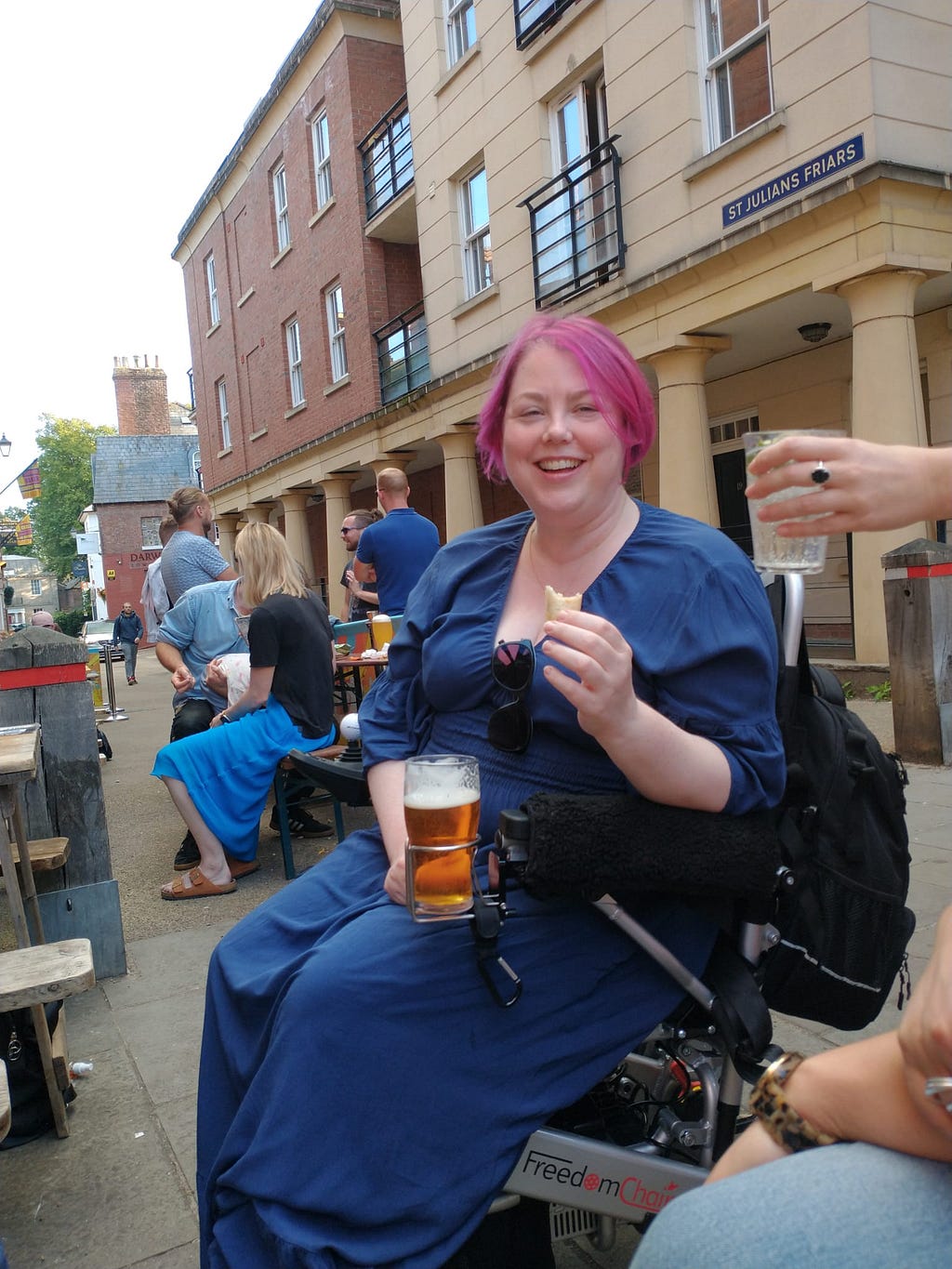 Claire sat in her electric wheelchair, with someone else's pint of beer in her chair's cupholder. Someone is handing her a gin and tonic.