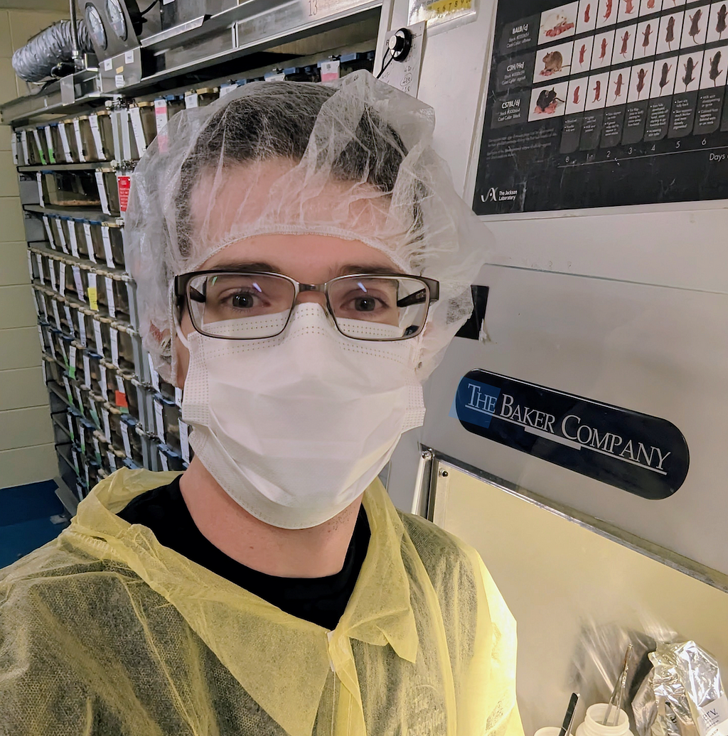 A man wearing glasses, a hair cover, and a face mask in a laboratory.
