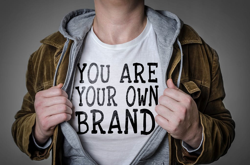 Man holding jacket open to show a t-shirt that says “You are your own brand”