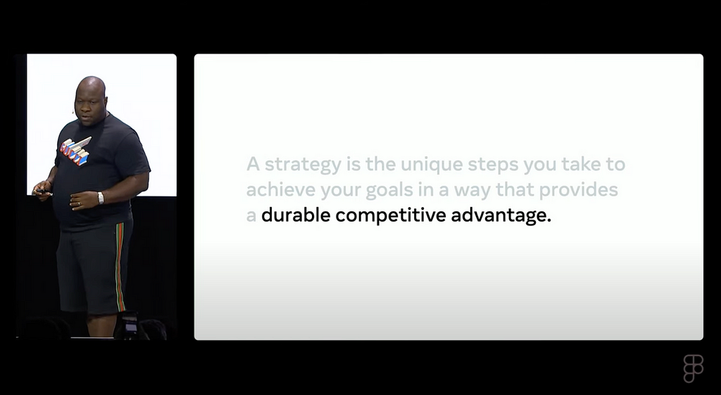 Dare Obasanjo, Product Manager at Meta, presents at Config 2024, standing next to a slide that reads “A strategy is the unique steps you take to achieve your goals in a way that provides a durable competitive advantage.”