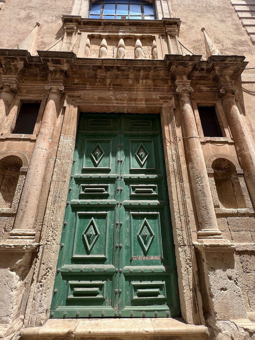 A large, green, ornate door to a baroque Sicilian building