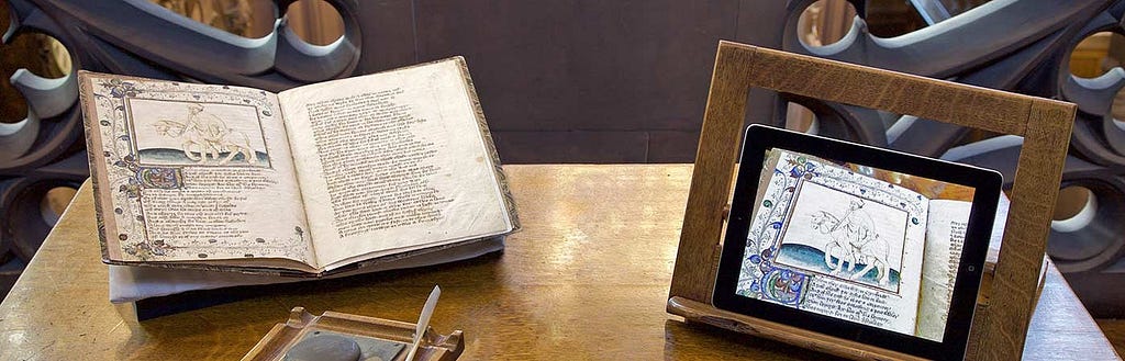 Old books and images of medieval illuminated manuscripts sit on a wooden desk.