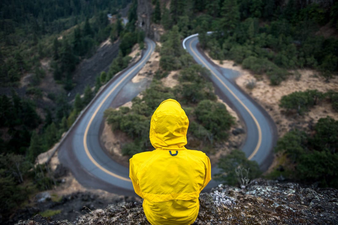person dressed in yellow rain jacket looking away at a road in the distance