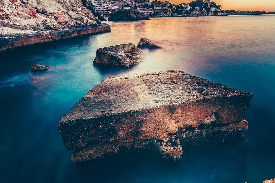 View of ocean with deep blue water and large rocks with city in the background.