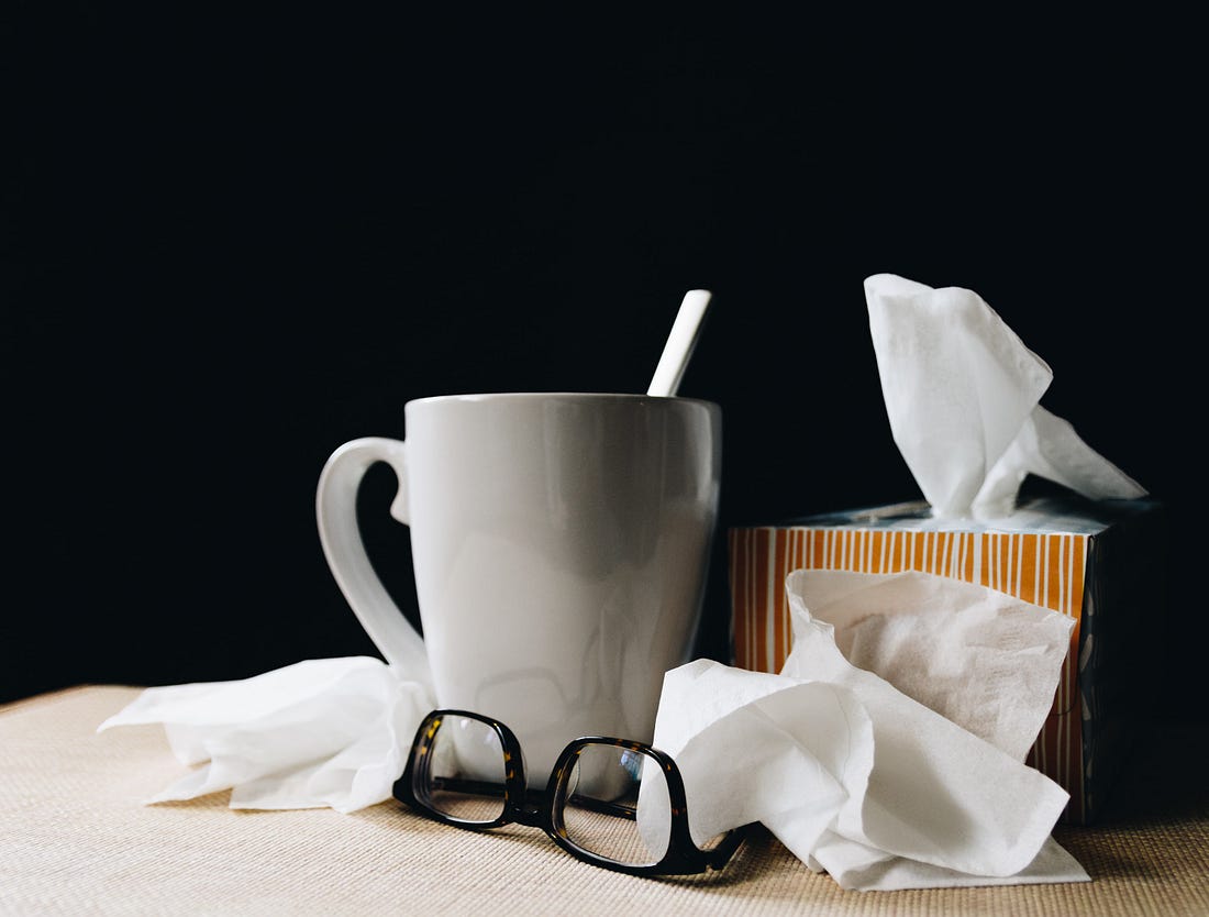 A pair of glasses, large mug, used tissue, and tissue box resting on a table.