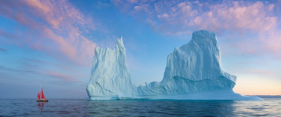 small red sailboat in front of iceberg