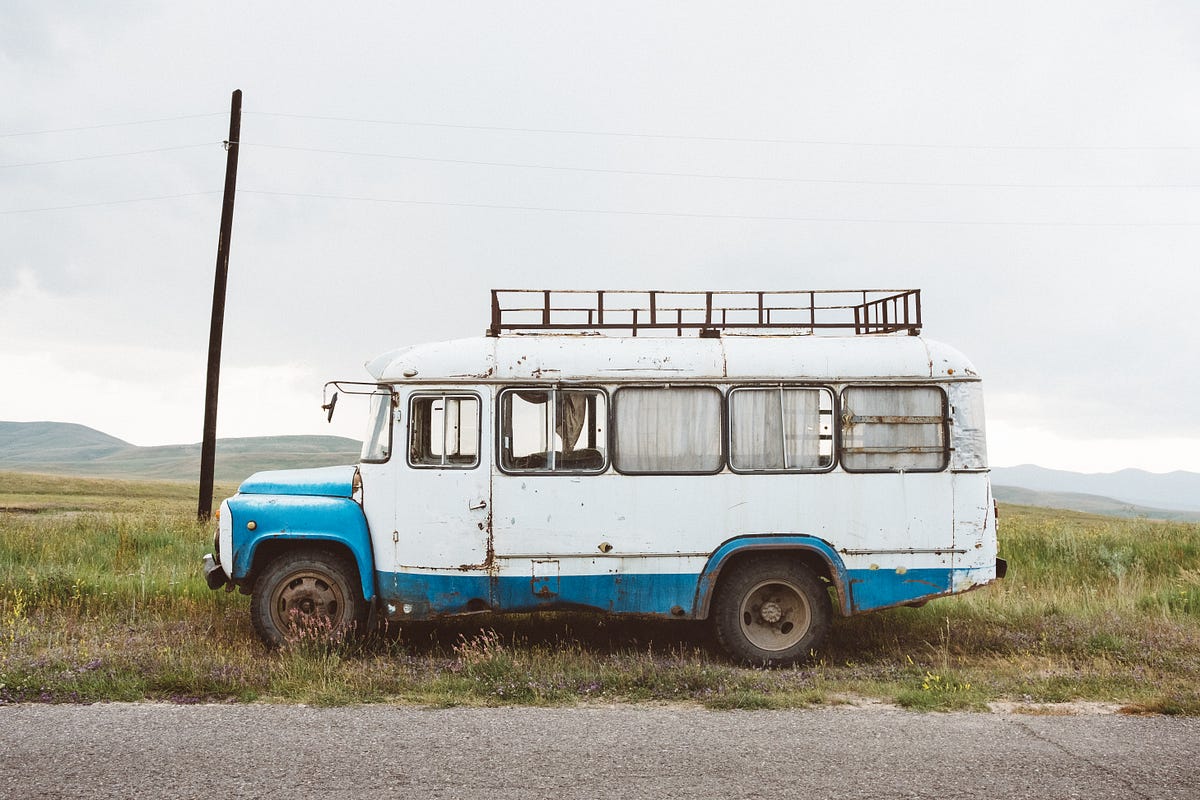 White and blue bus in the middle of a country road.