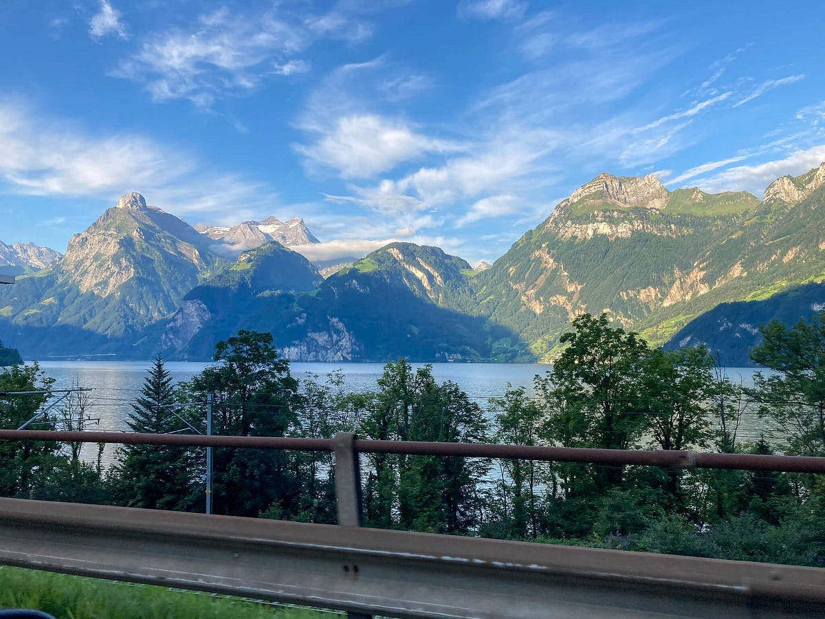 Picture of dramatic, tree-covered mountains behind an alpine lake. 