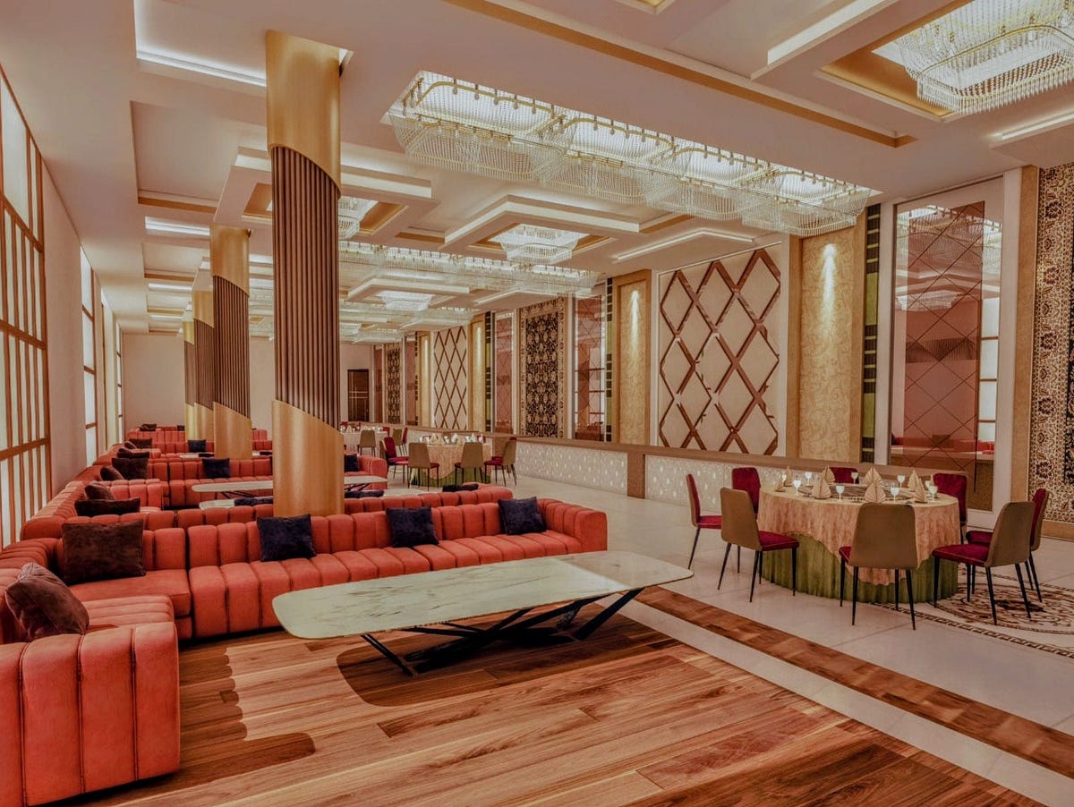 Luxurious banquet hall interior at DP Palace, Delhi, designed with warm wooden flooring, coral-toned sofas, contemporary ceiling lighting, and elegant pillar accents. This sophisticated layout is a testament to the finesse of the Best Interior Designer in Delhi, blending comfort and grandeur. A true showcase of how an Interior Designer in Delhi can elevate spaces into refined hospitality experiences.