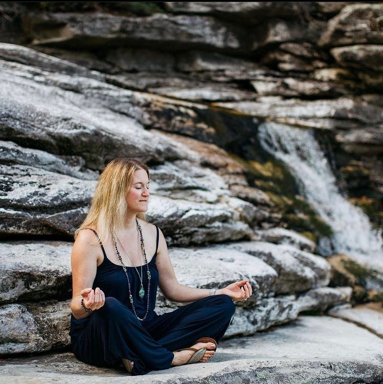 blonde woman meditating on a rock with waterfall in background