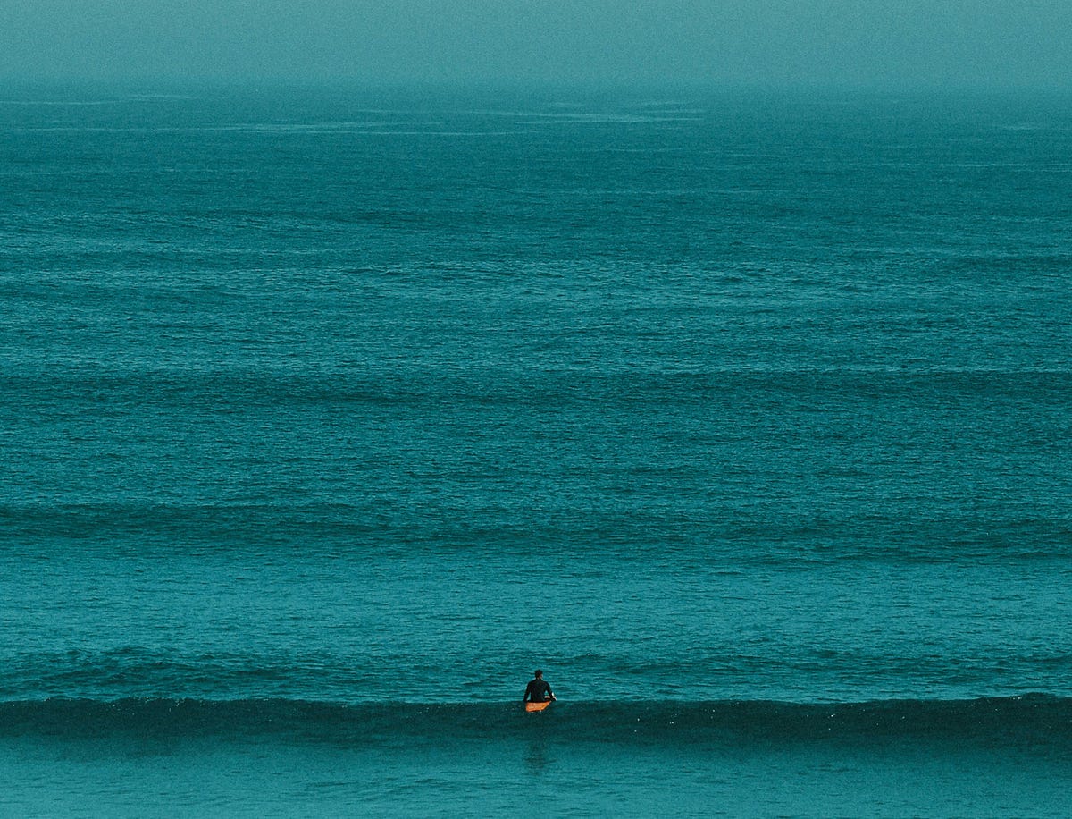 man sitting on surfboard over vast cyan ocean